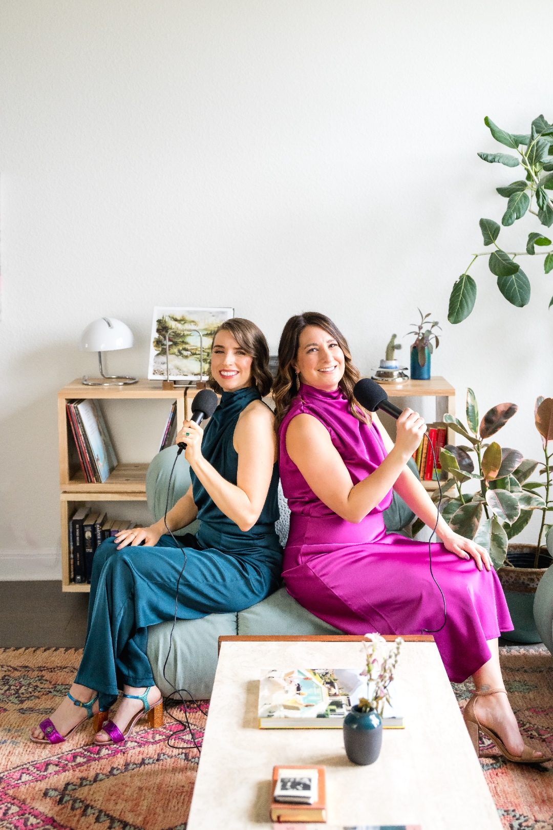 Robin Welch and Deborah Andrews sitting back-to-back holding microphones, hosts of the Art of Classiness podcast